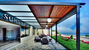Un espace extérieur aménagé, abrité et doté d’un sol en pierre, d’une pergola en bois et d’une vue sur l’océan.