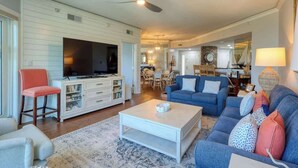 A living room with a television, sofas, a coffee table, and a dining area in the background.