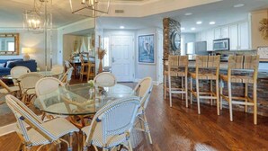A spacious dining area with a glass table and wicker chairs, a kitchen with white cabinets, and a stone accent wall.