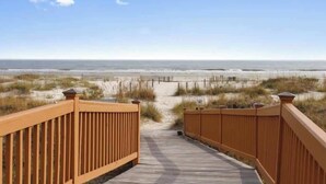 A wooden boardwalk leading to a beach with a clear sky.