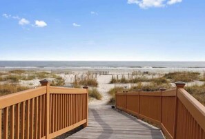 A wooden boardwalk leading to a beach with a clear sky.
