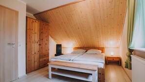 Une chambre avec un plafond en pente, une armoire en bois, une table de chevet, une lampe et un banc.