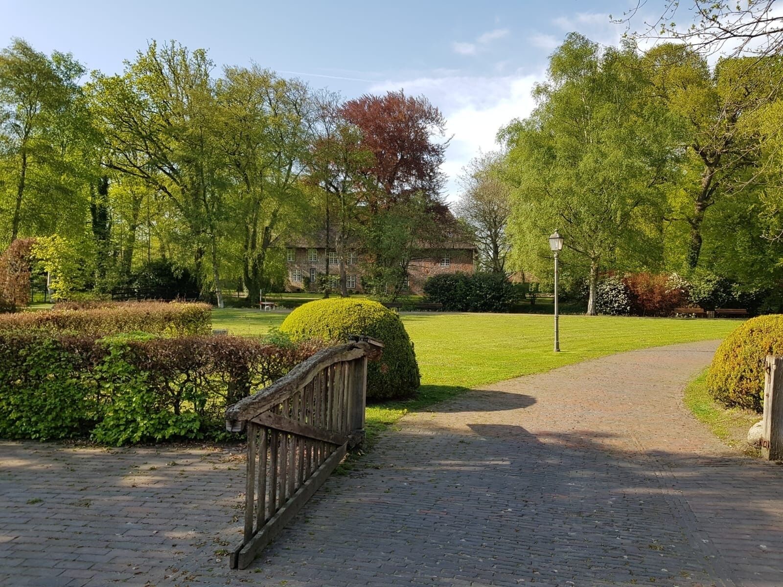 Un chemin pavé mène à un bâtiment entouré d’arbustes et d’arbres bien entretenus.