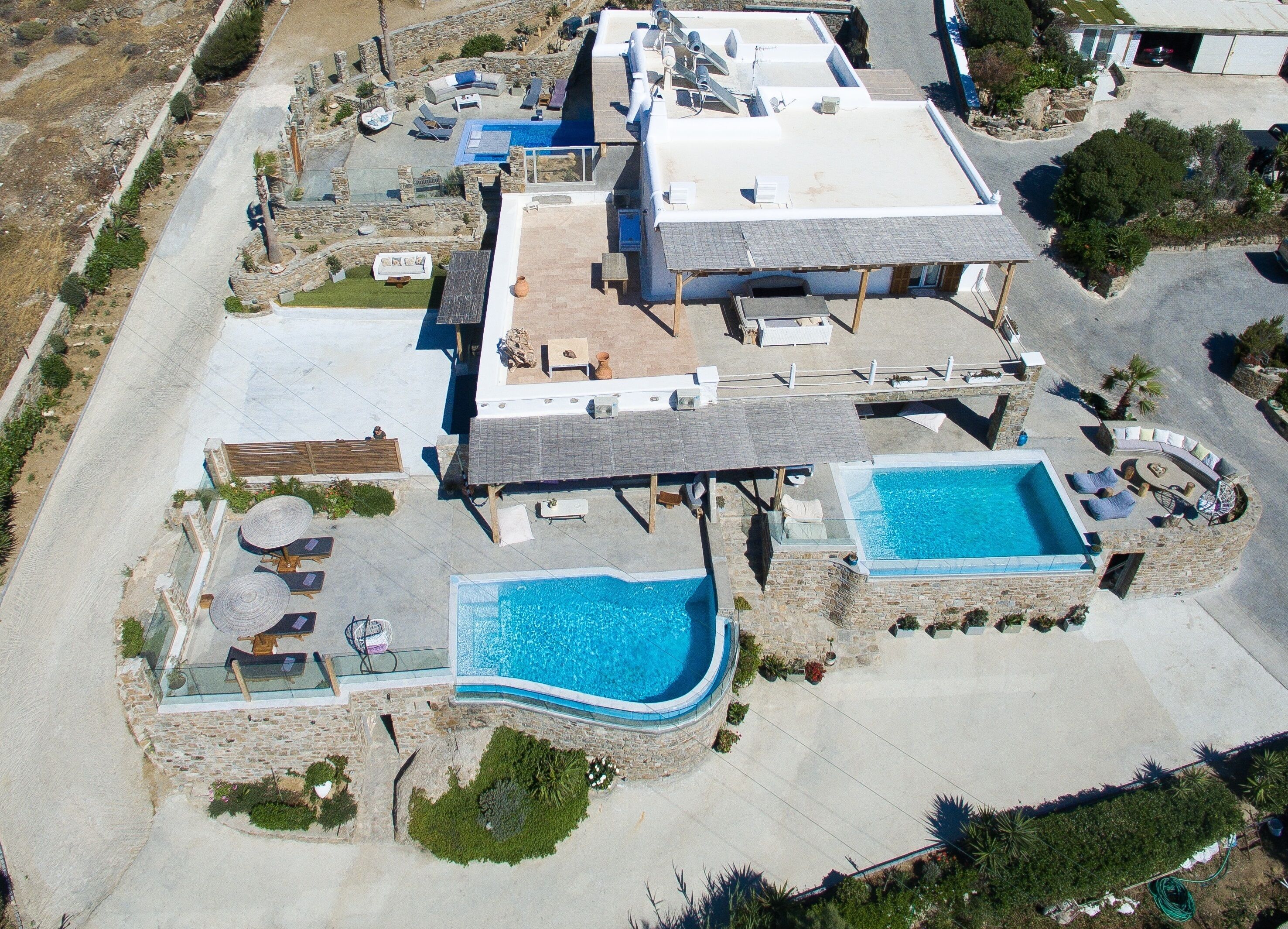 Vue aérienne d’un complexe hôtelier doté de deux piscines, d’espaces de détente en plein air et d’une terrasse sur le toit.