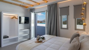 A modern bedroom with a large bed, a TV mounted on a white wall, a wooden ceiling, and a balcony view. - Mykonos Village (Mykonos)