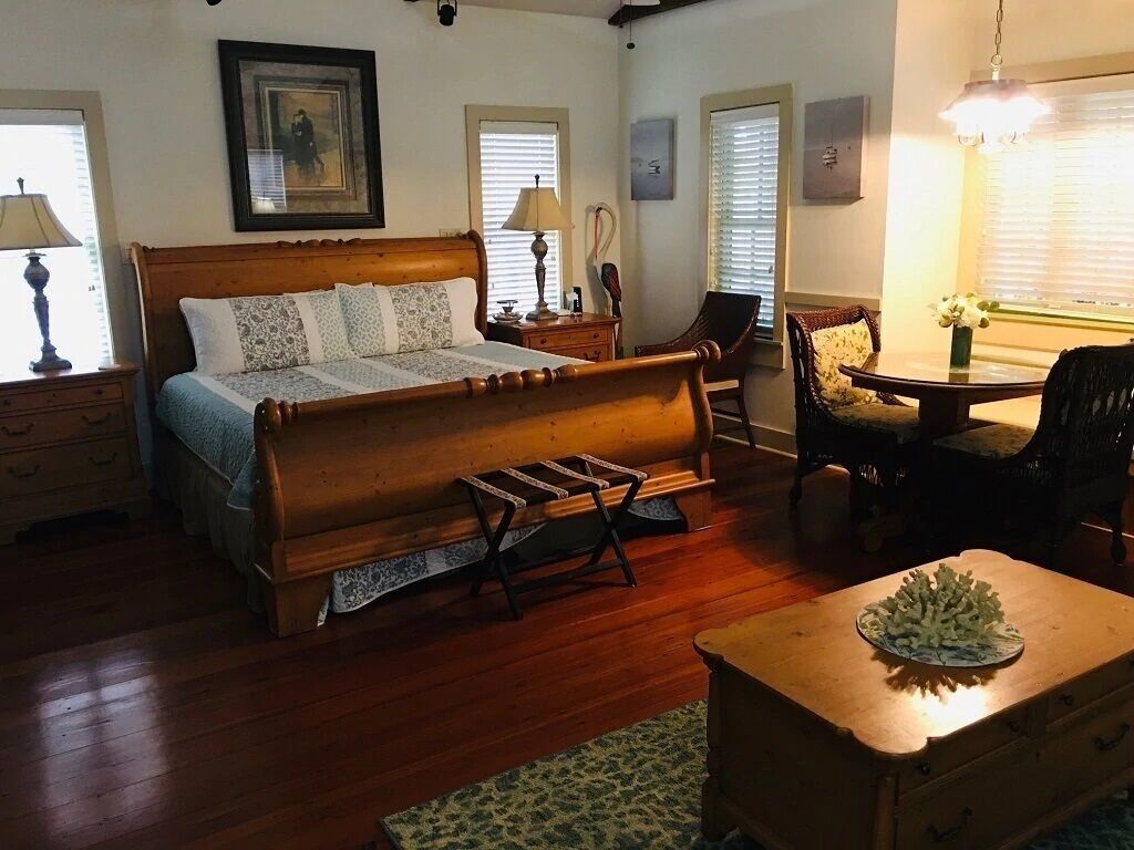 A bedroom with a wooden bed, bedside tables, a chair, a small table with a vase, and a window with blinds.