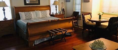 A bedroom with a wooden bed, bedside tables, a chair, a small table with a vase, and a window with blinds.