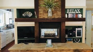 A living room with a stone fireplace, a television, and a bookshelf with a 'RELAX' sign.