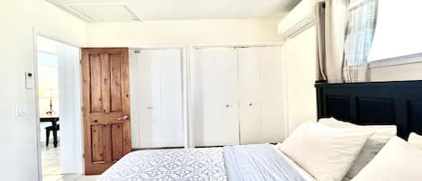 A bedroom with a bed, a ceiling fan, a window with curtains, and a door leading to another room.