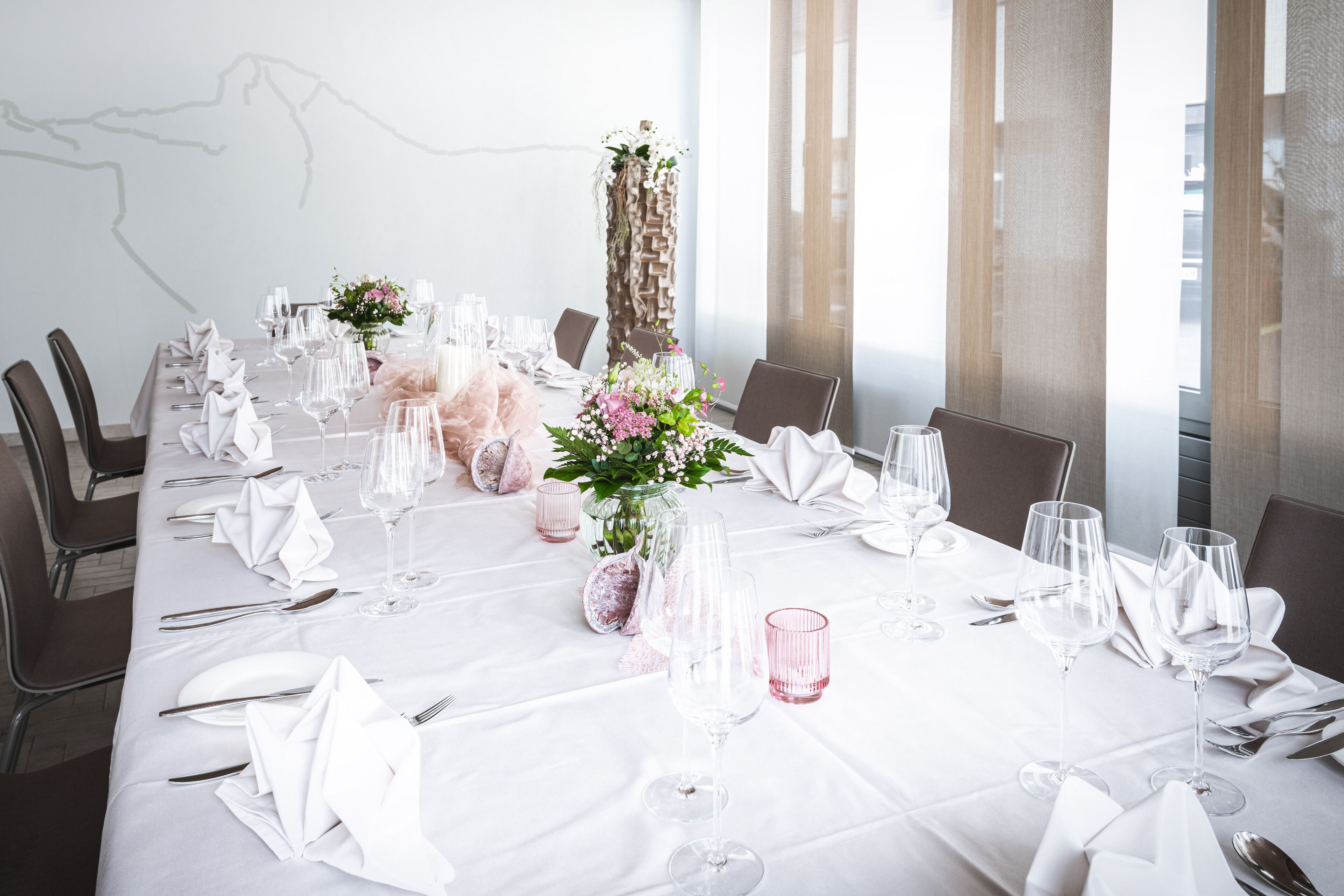 A dining table set for a formal event with white tablecloths, glassware, and floral centerpieces.