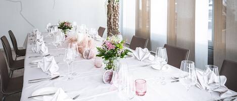 A dining table set for a formal event with white tablecloths, glassware, and floral centerpieces.