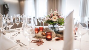 Une table à manger dressée avec des verres à vin, des couverts et des bougies, et un vase rempli de fleurs placé au centre.