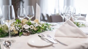 Une table dressée pour un dîner formel, avec des nappes blanches, de la vaisselle transparente et un centre de table composé de fleurs.
