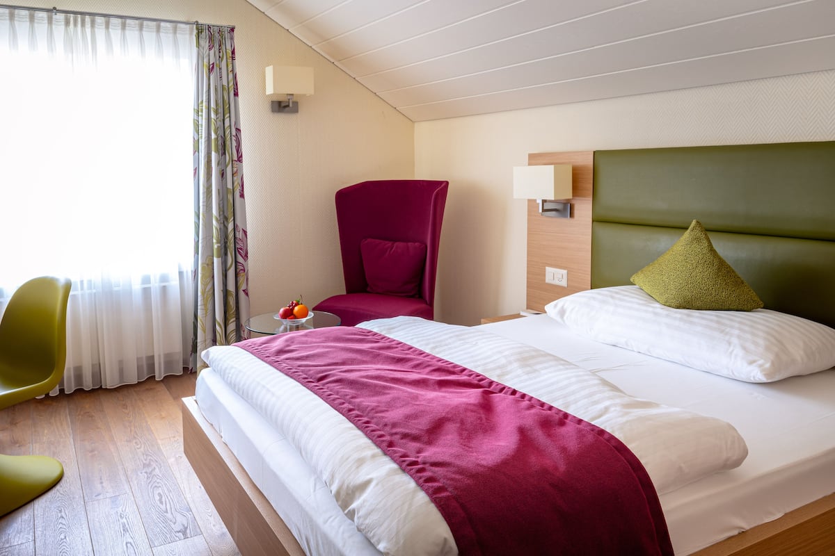 Habitación de hotel con cama, una silla, mesita de noche y ventana con cortinas.