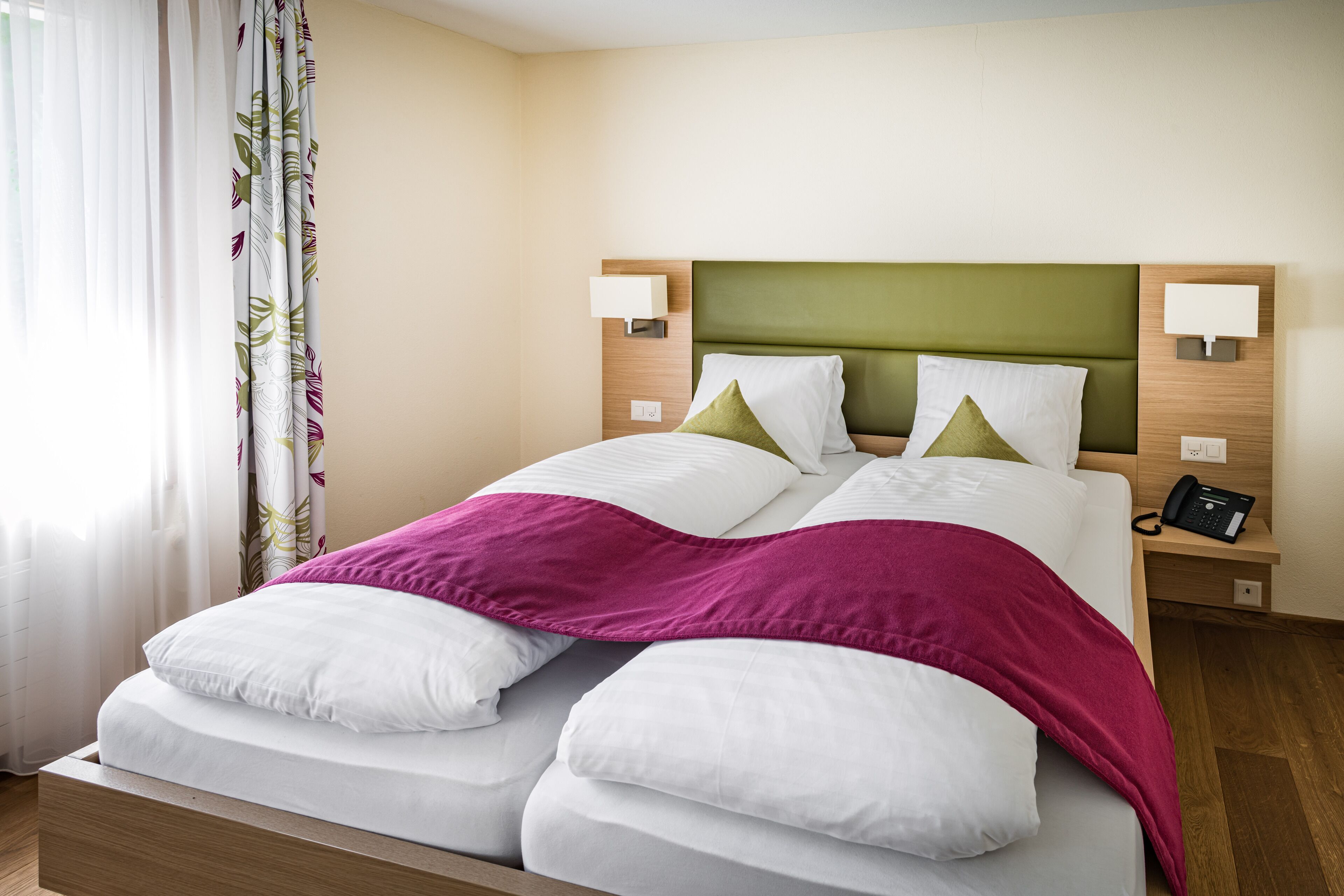 A hotel room with a bed, two bedside lamps, a telephone, and a curtain with a leaf pattern.