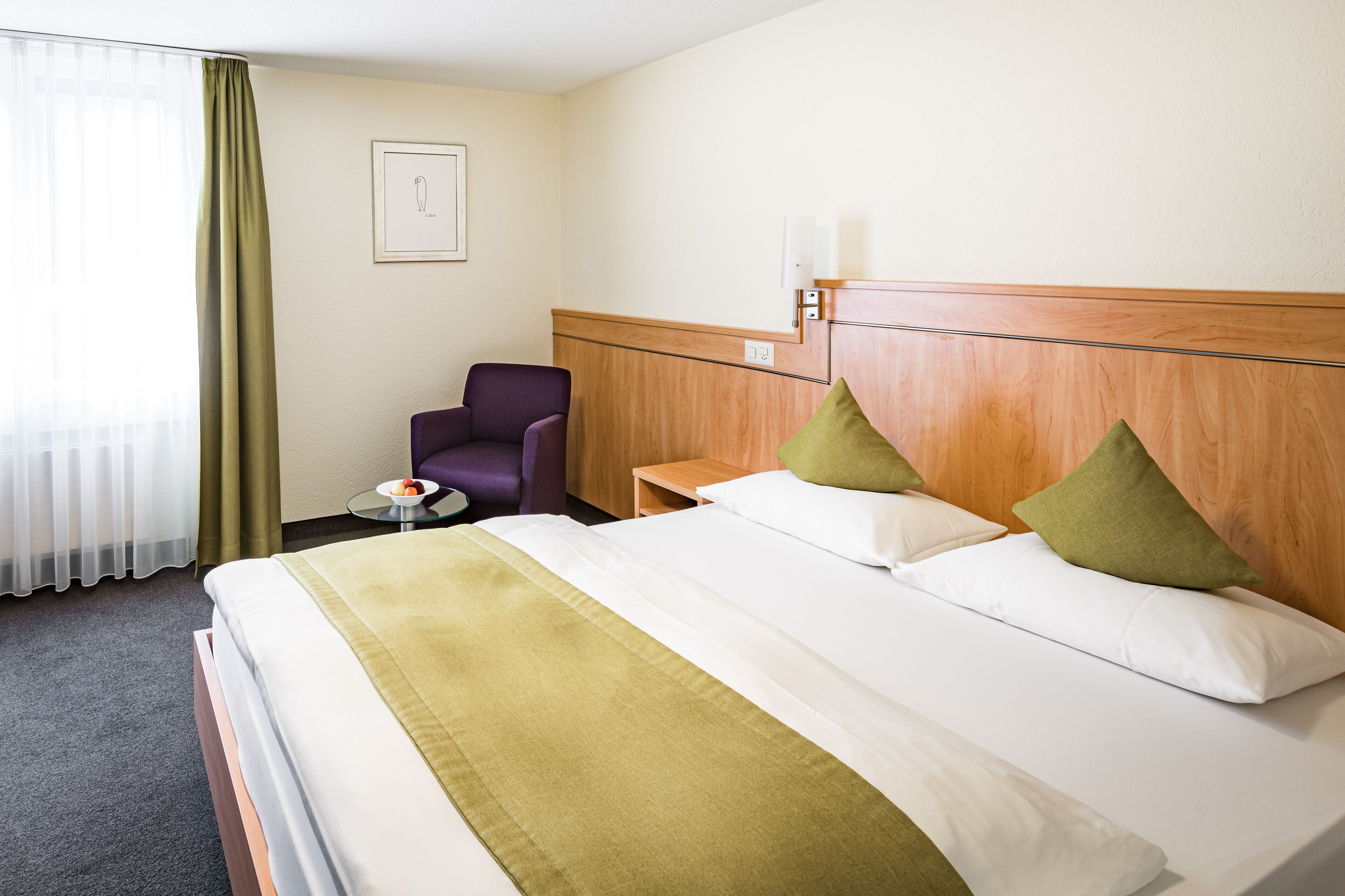 Hotellihuone, jossa on suuri sänky, tuoli, pieni pöytä ja ikkuna, jossa on verhot.