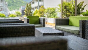 Mobilier d’extérieur en osier, agrémenté de coussins verts, placé devant un décor composé d’immebles et de verdure.