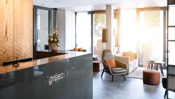 Un espace d’accueil moderne avec un comptoir en marbre, un mur à texture et un coin salon comprenant un canapé et des fauteuils.