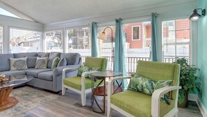 Una sala de estar con ventanales, un sofá gris, dos sillones verdes, una mesita y cortinas.