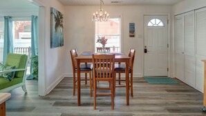 Un comedor con una mesa y sillas de madera, una araña y vistas al exterior.