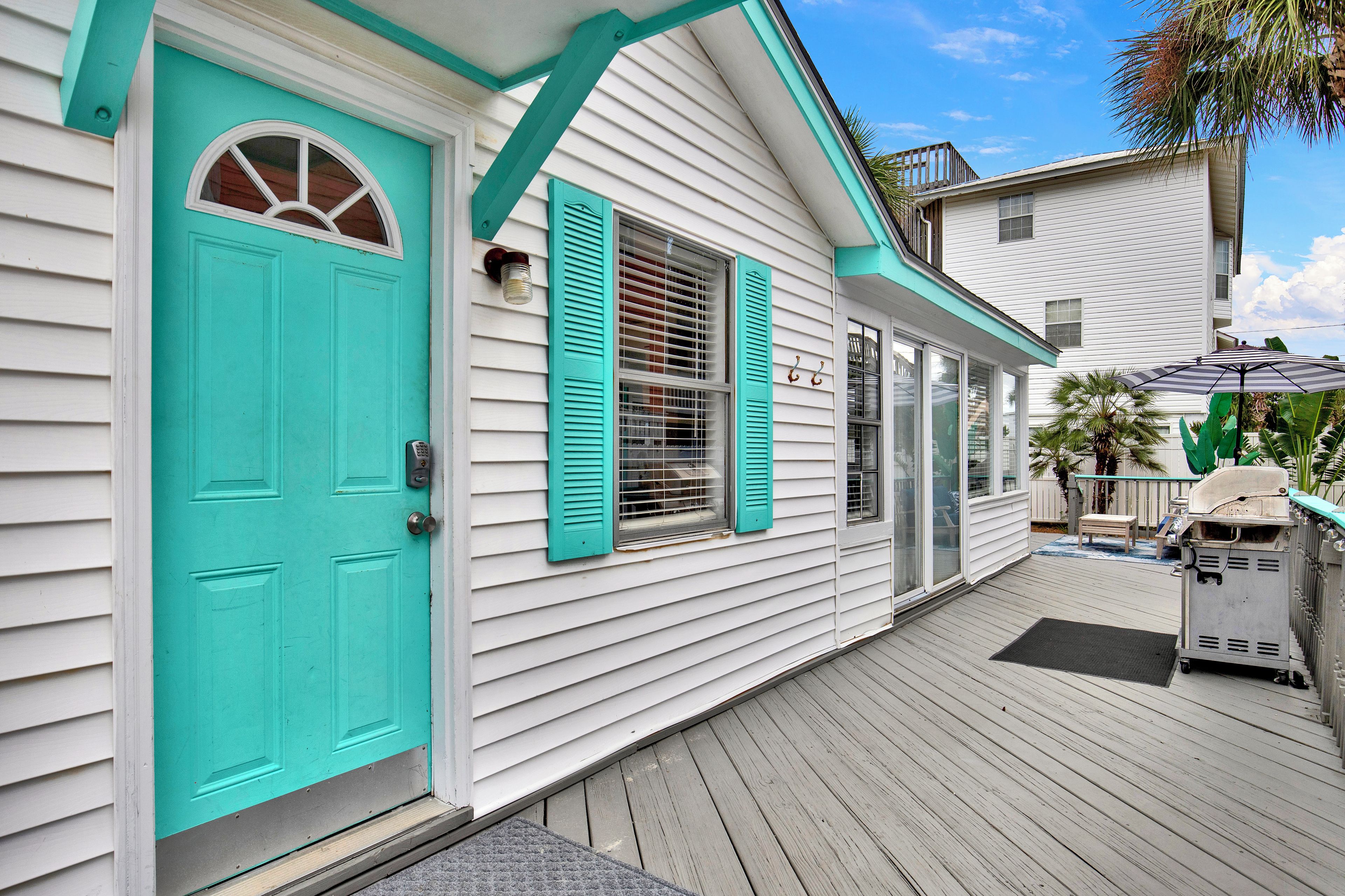 A house with a turquoise door, white siding, and a covered porch with a grill.