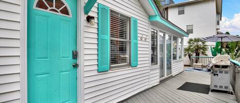 A house with a turquoise door, white siding, and a covered porch with a grill.