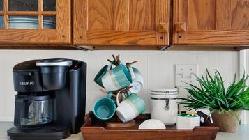 A kitchen with wooden cabinets, a Keurig coffee maker, a tray with mugs, a white appliance, and a potted plant.