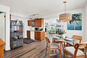 A modern kitchen with wooden cabinets, a dining area with a table set for two, and a view of the outdoors.