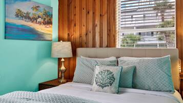A bedroom with a bed, pillows, a lamp, and a painting on the wall.
