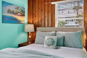 A bedroom with a bed, pillows, a lamp, and a painting on the wall.