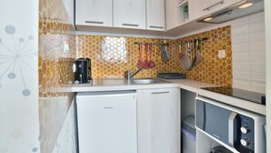 Una cocina compacta con gabinetes blancos, lavavajillas integrado, microondas y fregadero.