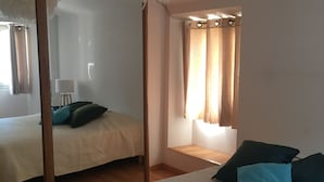 Een kamer met twee bedden, een hanglamp, een raam met gordijnen en een houten vloer.