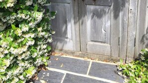 Una puerta de madera con un pestillo de metal, rodeada de flores blancas y follaje verde.