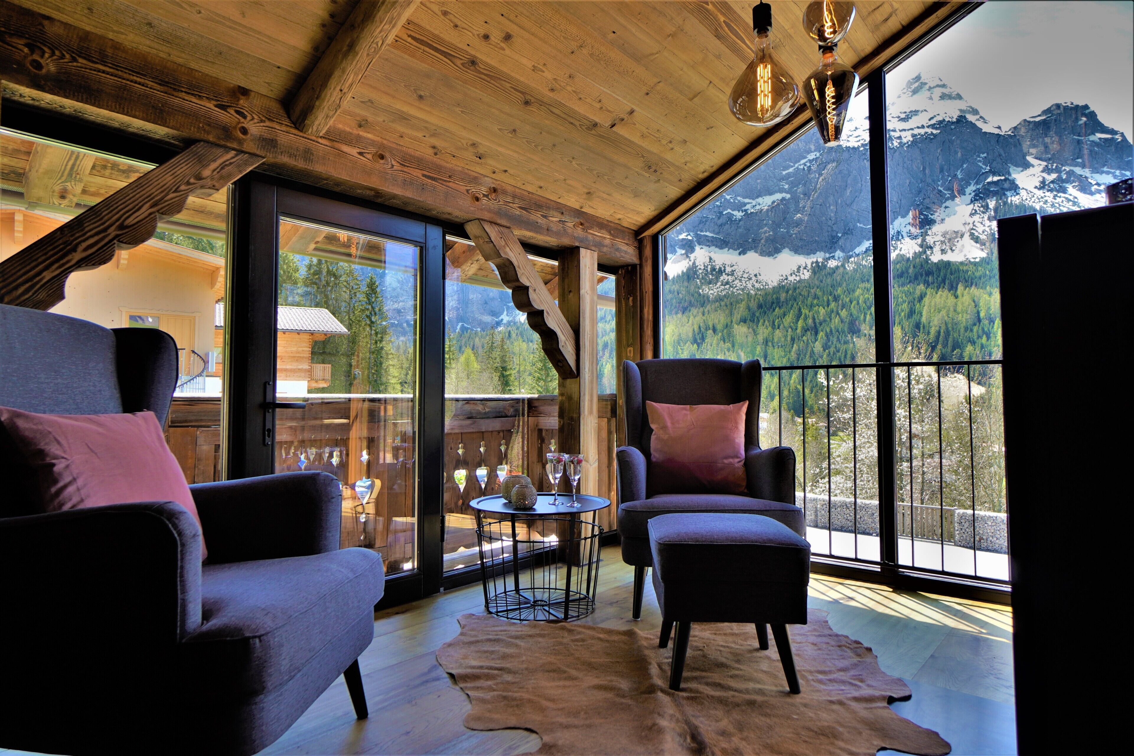 Ein gemütliches Zimmer mit Holzbalkendecke, großen Fenstern mit Blick auf die Berge und bequemen Sitzgelegenheiten.