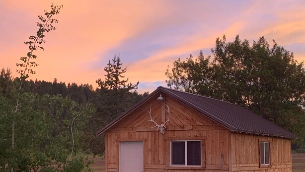 Una cabaña de madera con techo de metal, una puerta y una ventana.