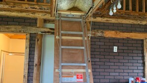 Una cocina estilo loft con una escalera de madera que lleva a un espacio para dormir elevado.