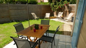 Een terras met een houten tafel en stoelen, een kleine tuin en een houten hek.