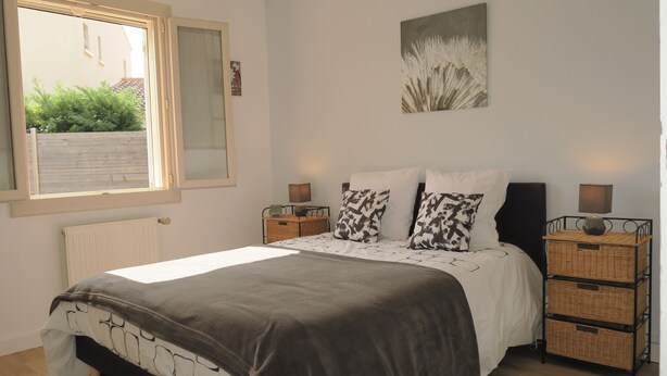 Een slaapkamer met een bed, twee nachtkastjes, een radiator, een raam en een aan de muur hangend schilderij.