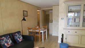 Een woonkamer met een zwarte bank, een klein bijzettafeltje, een spaarvarken en een boekenkast.