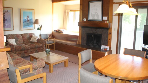A cozy living room with a fireplace, a sofa, a coffee table, and a dining table. - MOOSE-WILSON ROAD- WILSON, WY- PERFECT LOCATION AND GREAT FAMILY RETREAT! (Wilson)