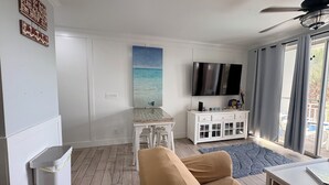 A living room with a beige sofa, a small table, a TV, and a window with curtains. - Coastal Condo with Amazing View & Beach Access (Santa Rosa Beach)