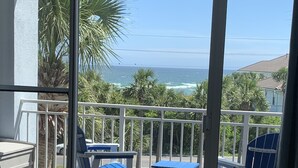 A balcony with a view of the ocean, featuring a table, chairs, and a small basket. - Coastal Condo with Amazing View & Beach Access (Santa Rosa Beach)