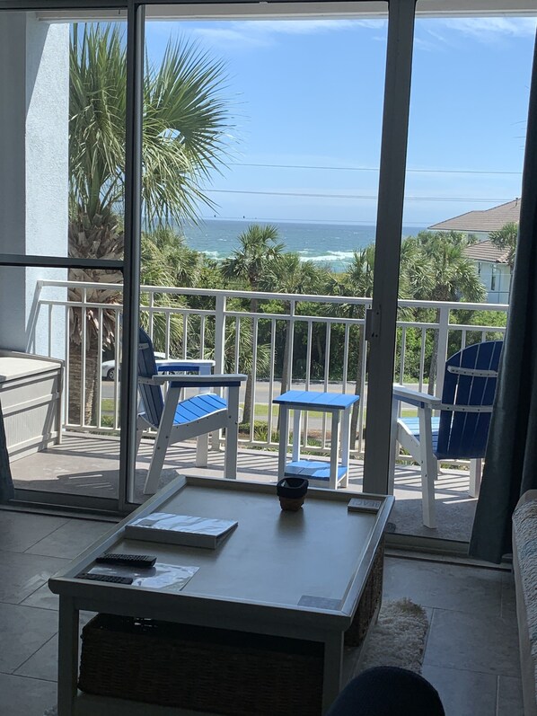 A balcony with a view of the ocean, featuring a table, chairs, and a small basket. - Coastal Condo with Amazing View & Beach Access (Santa Rosa Beach)