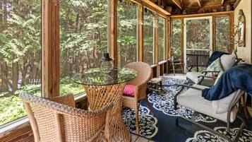 Une terrasse en bois avec des meubles en osier, une table en verre et un tapis à motifs.