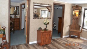 Een kamer met een houten kast, een spiegel en een stoel. Een deur leidt naar een andere kamer.