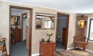 A room with a wooden cabinet, a mirror, and a chair. There is a door leading to another room. - Direct Betsie River frontage. (Thompsonville)