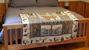 A bed with a quilt, a framed picture on the wall, and a rug on the floor. - Riverside Retreat  (Elkins)