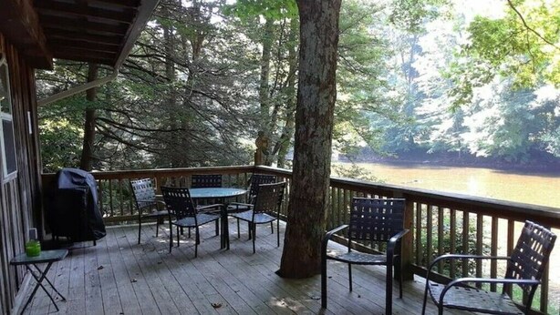 A wooden deck with outdoor seating and a view of a river. - Riverside Retreat  (Elkins)