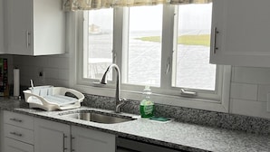 A kitchen with granite countertops, white cabinets, a dishwasher, a sink, and a window with a view of the water. - BEST BAYFRONT VALUE IN CHADWICK BEACH NEWLY RENOVATED SLEEPS 7 RATED 10/10 (Lavallette)