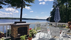 Une terrasse dotée d’une cheminée en pierre, de chaises blanches et offrant une vue sur un lac.